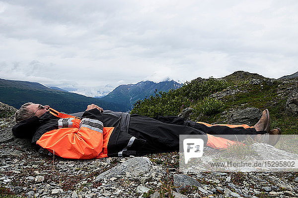 Älterer männlicher Wanderer  der auf dem Gipfel eines Berges liegend eine Pause macht  Seitenansicht  Valdez  Alaska  USA