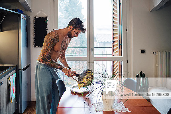 Mittelgroßer Mann mit Tätowierungen  der Omelett aus der Bratpfanne serviert