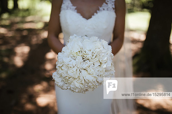 Junge Braut mit weißem Blumenstrauß im Wald  Mittelteil