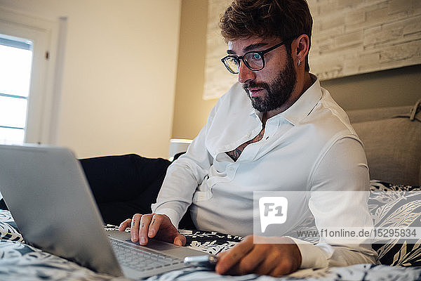 Mittelgroßer erwachsener Mann  der auf dem Bett liegt und auf einen Laptop schaut