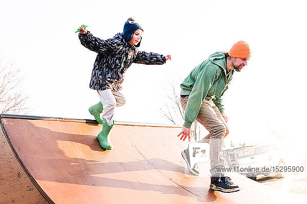 Junge jagt Vater auf Skateboard-Rampe hinterher  niedriger Blickwinkel