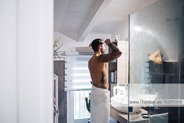 Mid adult man with tattoos combing hair at bathroom mirror