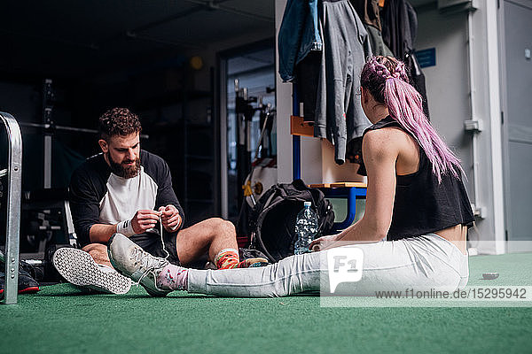 Frau spricht mit jungem Mann beim Schnürsenkelbinden im Fitnessstudio