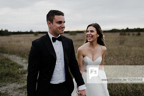 Glückliches junges Paar schlendert am Hochzeitstag Hand in Hand durchs Feld