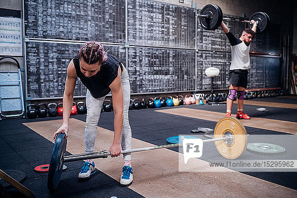 Young woman placing weight plate into bar in gym