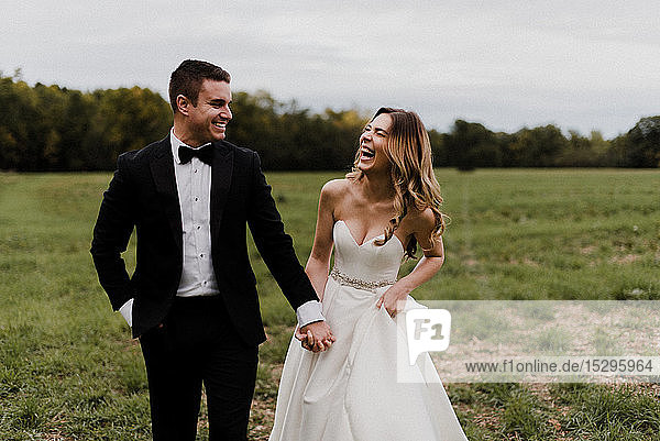 Romantic young bride and groom holding hands and laughing in field