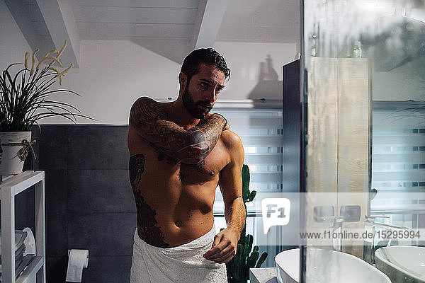 Mittelgroßer Mann mit Tätowierungen macht sich im Badezimmer fertig