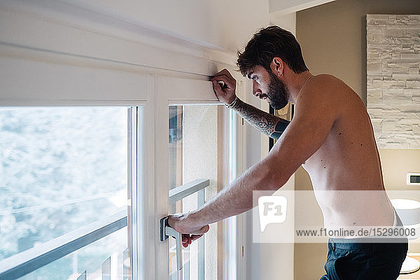Mittelgroßer erwachsener Mann  der durch ein Wohnungsfenster nach unten schaut