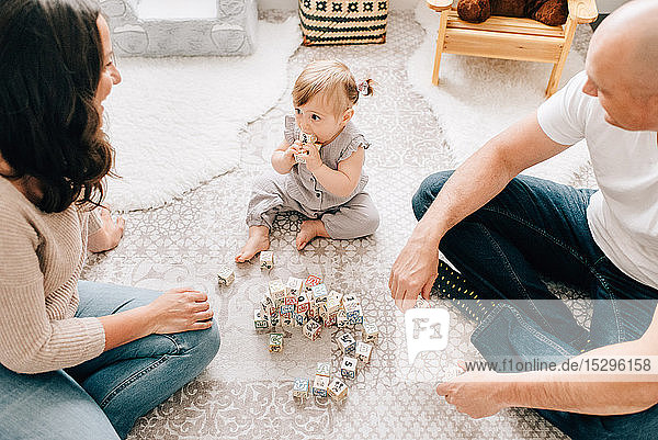 Mother and father sitting on nursery floor with baby daughter playing with building blocks