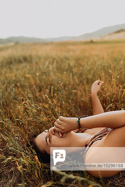 Junge Frau liegt lachend auf einem Feld aus langem Gras  Exeter  Kalifornien  USA