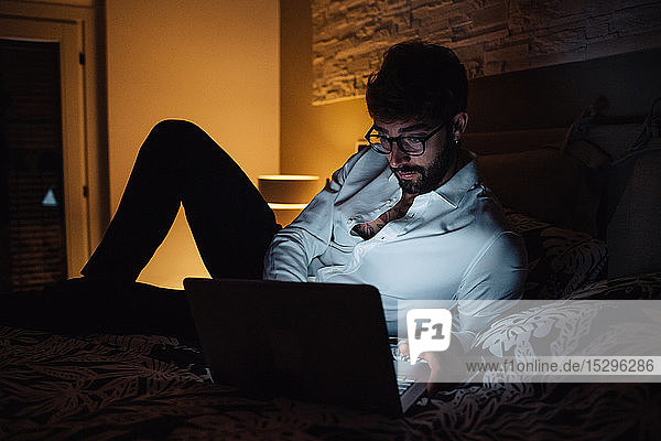 Mittelgroßer erwachsener Mann  der nachts mit einem Laptop auf dem Bett liegt