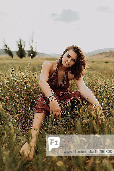 Beautiful young woman sitting in field of long grass  portrait  Exeter  California  USA