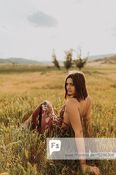 Hübsche junge Frau sitzt auf einem Feld aus langem Gras und schaut über ihre Schulter  Porträt  Exeter  Kalifornien  USA
