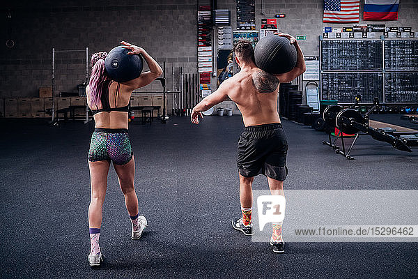 Junge Frau und Mann trainieren zusammen  tragen den Atlasball auf den Schultern in der Turnhalle  Rückansicht