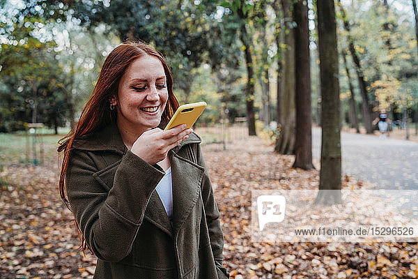 Junge Frau mit langen roten Haaren beim Smartphone-Selfie im Herbstpark