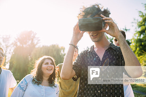 Gruppe von Freunden beobachtet Mann  der im Park in ein VR-Headset schaut