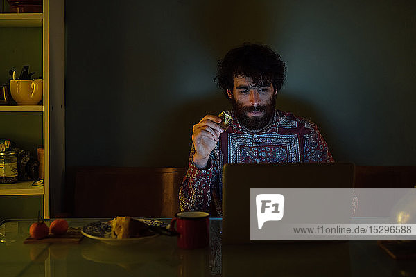 Bärtiger junger Mann frühstückt mit Laptop zu Hause