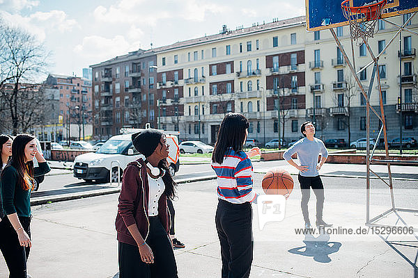 Junge weibliche und männliche erwachsene Freunde spielen Basketball auf dem Stadtplatz
