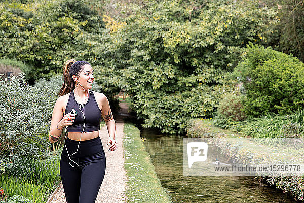Young female runner listening to earphones while running on riverside path