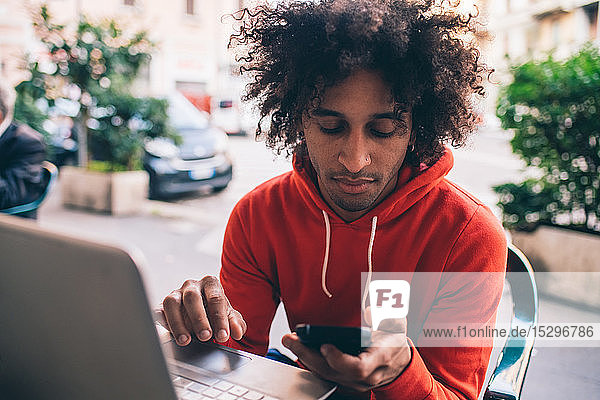 Junger Mann benutzt Smartphone und Laptop im Café