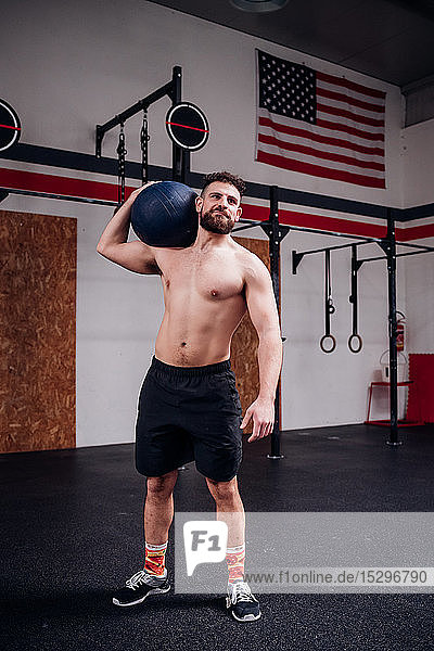 Young man training  carrying atlas ball on shoulder in gym