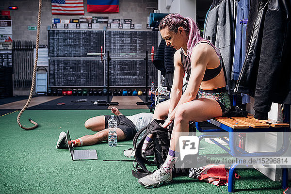 Junge Frau trainiert  sitzt auf Bank und packt Sporttasche im Fitnessstudio