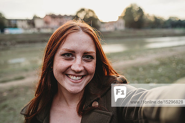 Young woman with long red hair smiling for selfie on riverside  personal perspective  Florence  Tuscany  Italy