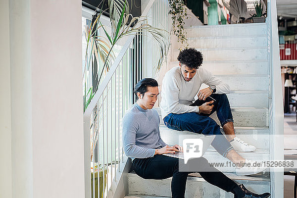 Junge Geschäftsleute sitzen mit Laptop auf der Treppe