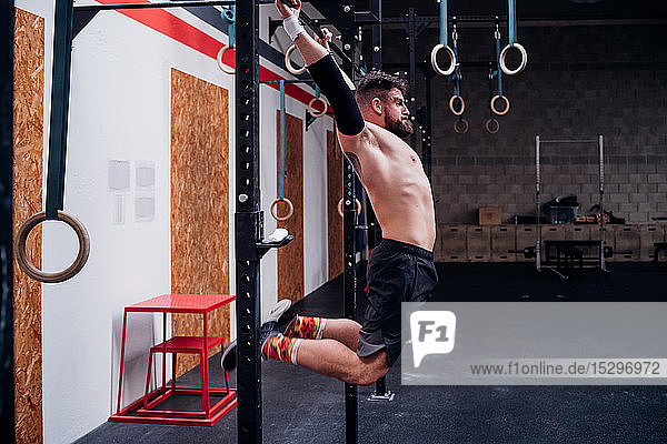 Bare chested young man training  swinging on exercise bar in gym