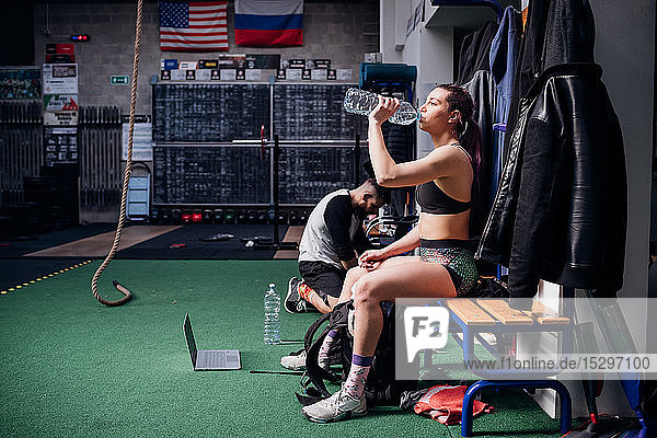 Junge Frau trainiert  sitzt auf einer Bank und trinkt Wasser in Flaschen im Fitnessstudio