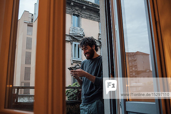 Bärtiger junger Mann benutzt Smartphone auf dem Balkon
