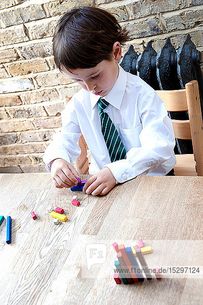 Junge in Schuluniform spielt zu Hause mit farbigen Stöcken