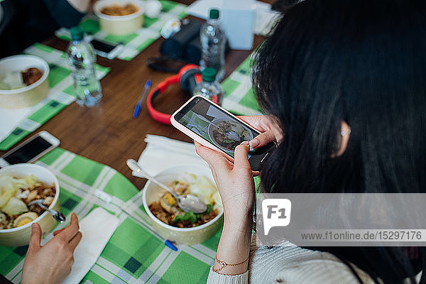 Junge Frau beim Fotografieren des Essens am Café-Tisch  Blick über die Schulter