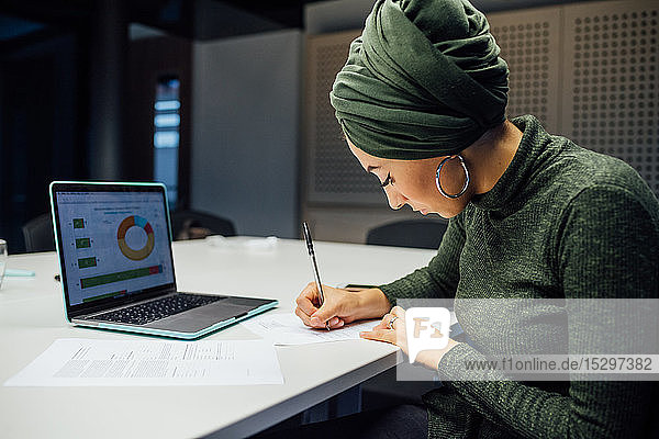 Businesswoman writing notes and using laptop in office