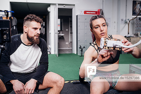 Junge Frau und Mann trainieren zusammen und stellen die Steuerung des Rudergeräts im Fitnessstudio ein