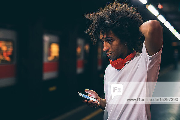 Junger Mann benutzt Smartphone auf Bahnsteig