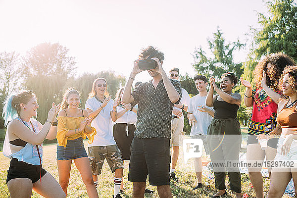 Group of friends watching man looking into VR headset in park