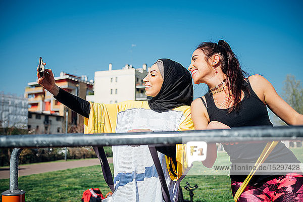 Calisthenics-Kurs im Outdoor-Fitnessstudio  zwei junge Frauen beim Smartphone-Selfie