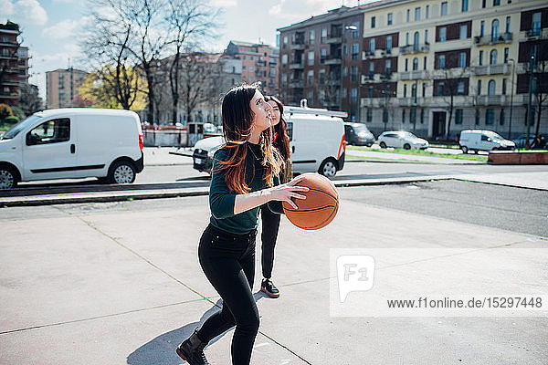Young female friends playing basketball on city court