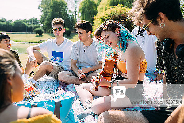 Group of friends relaxing  playing guitar at picnic in park