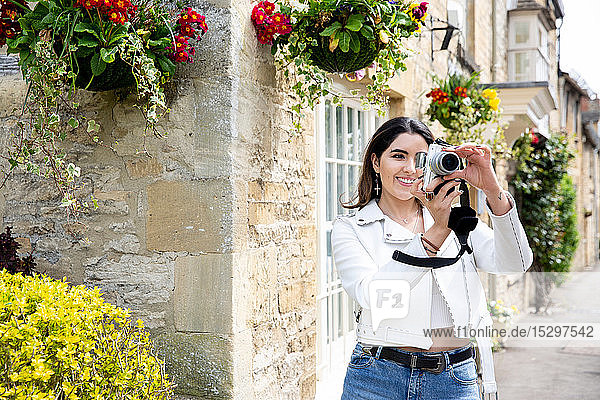 Young woman on village street photographing with digital camera  Cotswolds  England