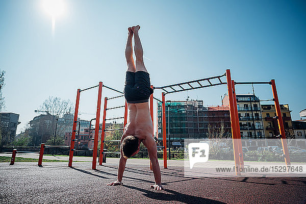 Gymnastik im Fitnessstudio im Freien  junger Mann beim Handstand  Rückansicht