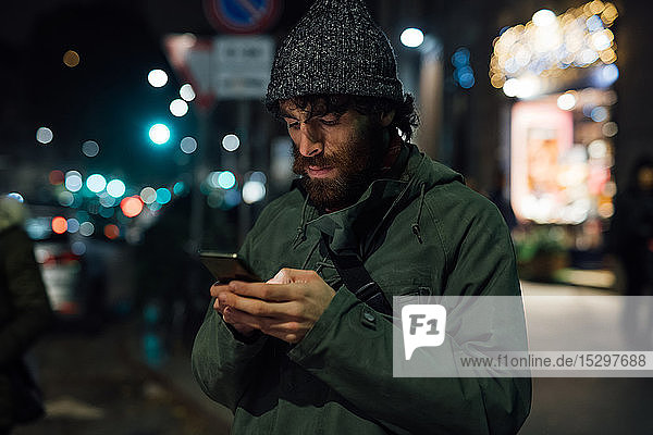 Bärtiger junger Mann benutzt Smartphone auf der Straße