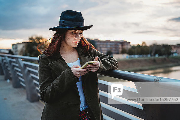 Young woman with long red hair on footbridge looking at smartphone at dusk  Florence  Tuscany  Italy