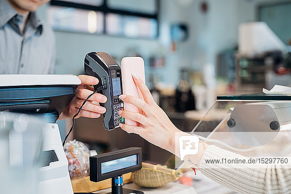 Junge Geschäftsfrau beim Bezahlen per Smartphone an der Cafe-Theke  beschnitten
