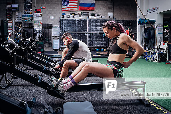 Junge Frau und Mann trainieren zusammen und bereiten sich auf den Gebrauch von Rudergeräten im Fitnessstudio vor