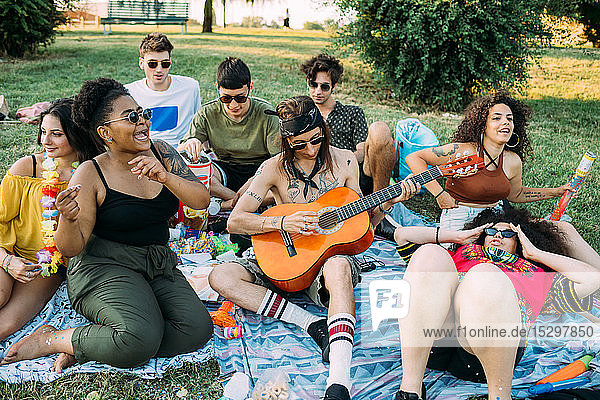 Gruppe von Freunden entspannt sich  spielt Gitarre beim Picknick im Park