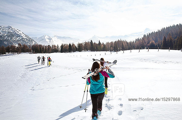 Five teenage girl skiers carrying skis in snow covered landscape  rear view  Tyrol  Styria  Austria