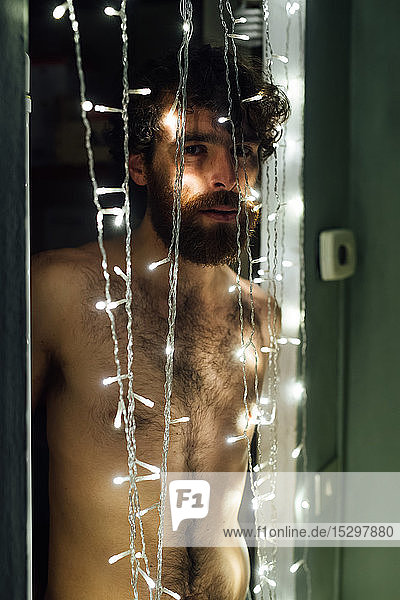 Bärtiger junger Mann steht hinter einer dekorativen Lichterkette