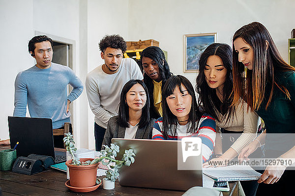 Gruppe junger Geschäftsfrauen und -männer betrachtet Laptop in Bürobesprechung